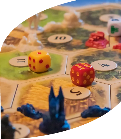 Een close-up van het bordspel „De Kolonisten van Catan“ tijdens het spel. Op zeshoekige tegels staan grondstoffen en genummerde speelstukken afgebeeld. Rode en blauwe speelstukken en dobbelstenen liggen verspreid over het bord.